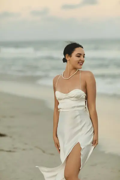 Uma jovem mulher em um vestido branco sorri enquanto caminha ao longo de uma praia de areia em Miami. — Fotografia de Stock