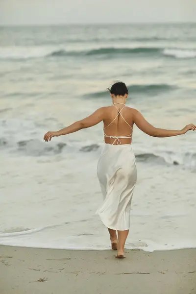 A young woman in a white dress walks along the sandy shore of Miami Beach. — Stock Photo