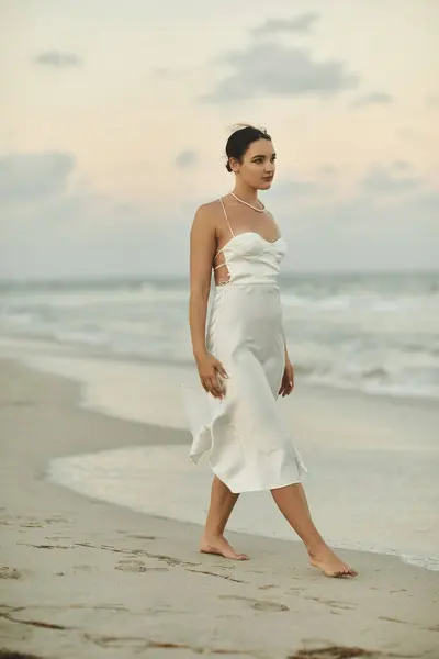 A woman in a white dress walks barefoot on a sandy beach in Miami. — Stock Photo