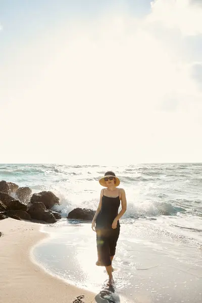 A woman in a dress walks along a sandy beach in Miami, with the ocean waves crashing behind her. — Stock Photo