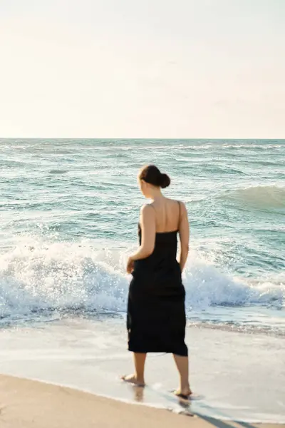 A woman wearing a black dress walks along Miami Beach, Florida, gazing out at the crashing waves. — Stock Photo