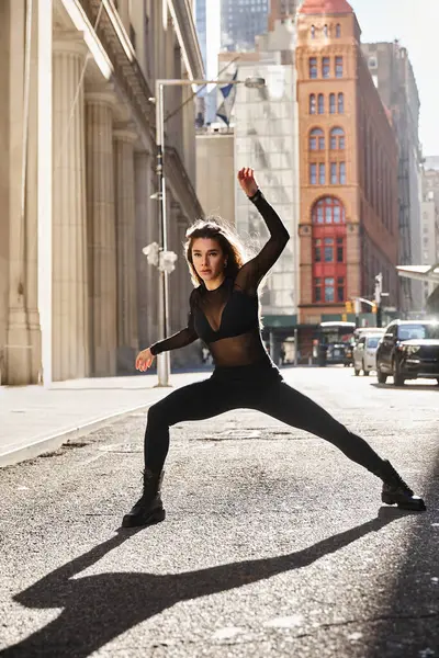 Una joven baila en una calle de Nueva York, su sombra se extiende por el pavimento. - foto de stock
