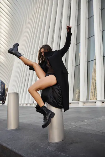 A young woman in a black coat dances on a street in New York City, her leg outstretched. — Stock Photo