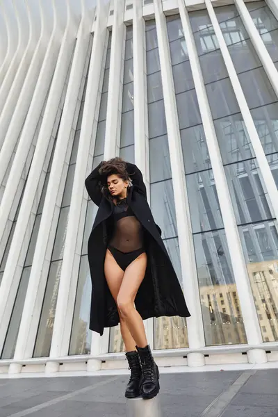 Woman in black bodysuit and coat dances by NY glass building. — Stock Photo