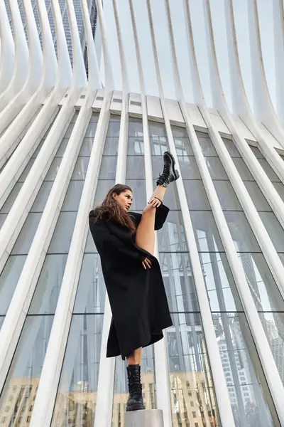 In NYC, a young woman dances gracefully, contrasting with the surrounding architecture. — Stock Photo