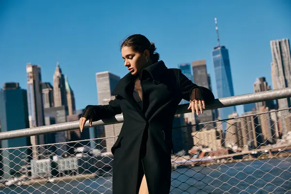 A young woman stands on a railing, looking out at the Manhattan skyline. — Stock Photo