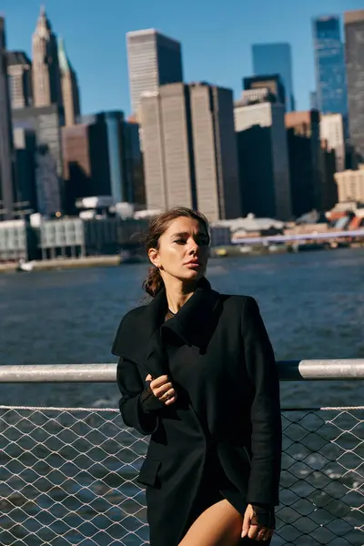 Una joven se para en un muelle de Nueva York, mirando el horizonte de la ciudad. - foto de stock