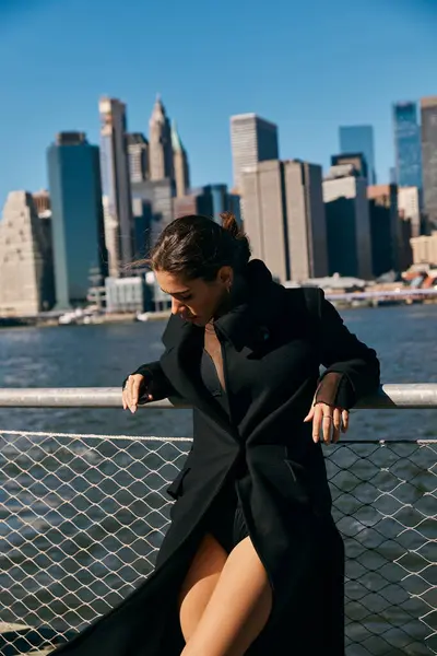 A woman in a black coat dances on a pier in New York City, with the skyline in the background. — Stock Photo