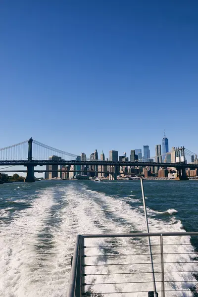 A view of the New York City skyline from the water, with a bridge in the foreground. — Stock Photo