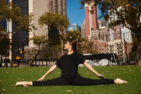 A young woman performs a split on a grassy park in the heart of New York City. — Stock Photo