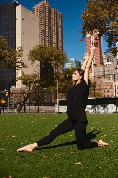 Una joven vestida de negro realiza un elegante movimiento de baile en un campo de hierba en la ciudad de Nueva York. - foto de stock