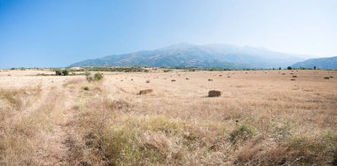 At first glance, an unkempt wide field with straw bales. Bulgarian mountains in the background. Blue sunny sky.