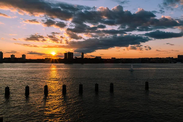 A yacht sails in the river during sunset over the city