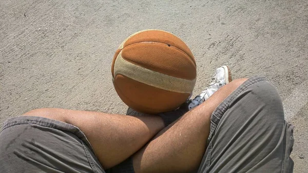 A boy is sitting on concrete floor with his basketball