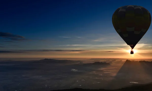 A balloon silhouette is flying over a mountain range in sunrise time