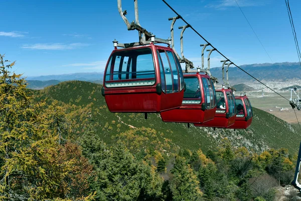 Red cable car over a green pine hill in a sunny day