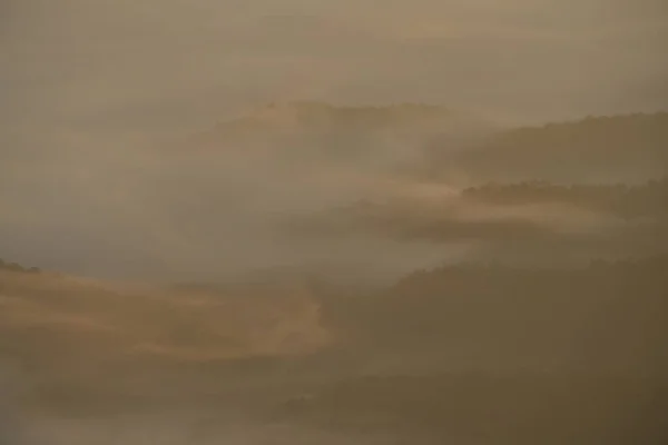 Dense fog is flowing over a hill in a morning
