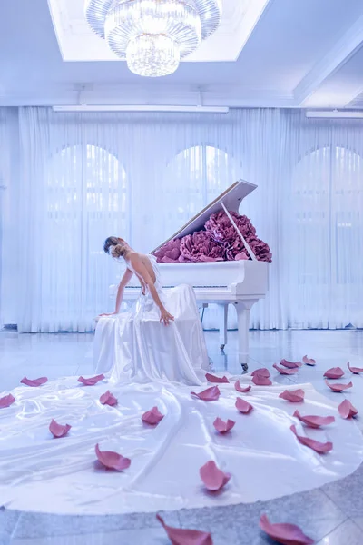 stock image Beautiful woman with white piano and peonies flowers in white studio