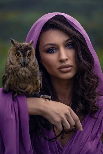 Beautiful woman with owl in purple dress in nature