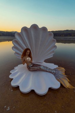 Devasa deniz kabuğu olan güzel kızıl saçlı kadın.