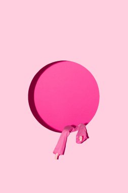Pembe pantolonlu bir bebeğin bacakları, pastel pembe bir duvardaki yuvarlak bir delikten sarkıyor. Yaratıcı asgari kavram.