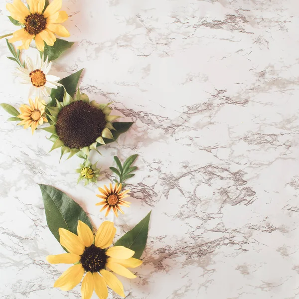 Creative flower layout with sunflowers, and leaves on bright marble table background. Minimal healthy food concept. Flat lay.
