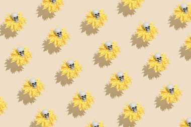 Sarı çiçeklerin üzerinde yüzen ve bej arka planda yükselen küçük insan kafatası deseni. Yaratıcı Cadılar Bayramı ya da Santa Muerte konsepti. Ürkütücü parti arkaplanı. Düz yatış, üst görünüm.