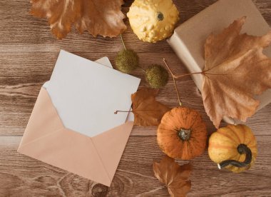 Balkabakları, düşen yapraklar ve açık bir zarfla ahşap masa üzerinde yaratıcı sonbahar kompozisyonu. Uzayı kopyala, düz yat