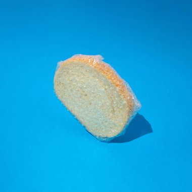 Mavi arka planda folyoya sarılı susam tohumlu taze beyaz ekmek dilimi. Fırın kavramı