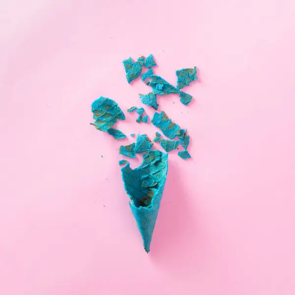 Shattered blue ice cream cone on pastel pink background. Minimal food concept. Flat lay.