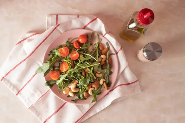 Harvested arugula, cherry tomatoes, almond, cashew on a pink plate in a kitchen marble table. Food ingredients concept