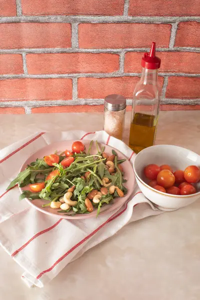 Harvested arugula, cherry tomatoes, almond, cashew on a pink plate in a kitchen marble table. Food ingredients concept