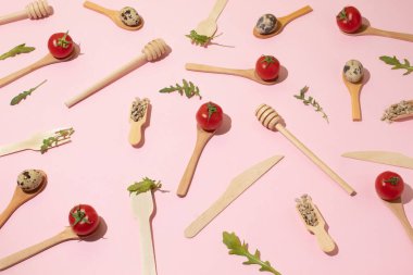 Ahşap mutfak çatal bıçak takımı, kiraz domatesleri, bıldırcın yumurtaları, pembe arka planda ayçekirdeği. Düz uzanma deseni