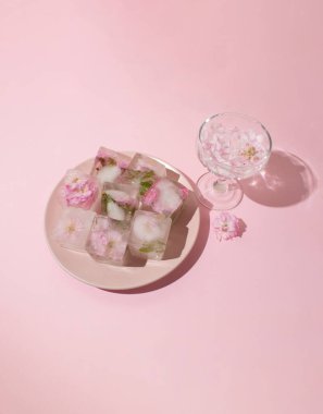 Buz küplerinde güzel pembe çiçekler ve pembe arka planda pembe tabakta taç yaprakları olan cam, üst manzara.