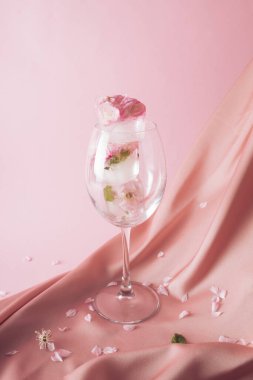 İçecekte eriyen çiçekli buz küpleri arka plandaki ipeksi pembe kumaş üzerinde.