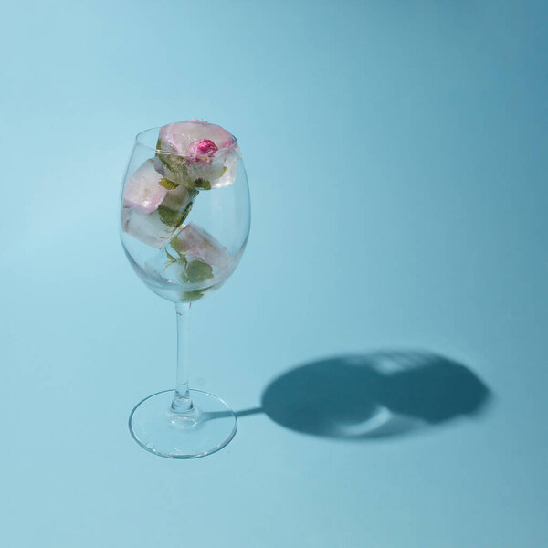 Beautiful small pink flowers in transparent glass on blue background with copy space