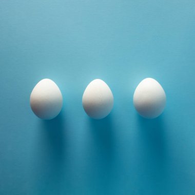 Mavi arka planda üç beyaz yumurta - düz yatıyordu