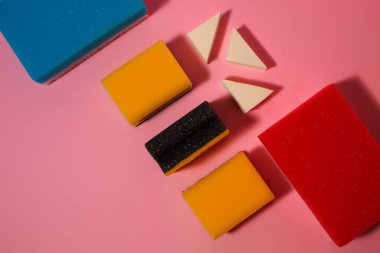 Pastel pembe arka plandaki süngerleri temizlemekten gelen yaratıcı bir düzenleme. Yaratıcı desinasyon fikri.