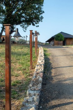 Çiftlikteki bir patikanın yanında lambalar olan tahta direkler. Güneşli bir gün