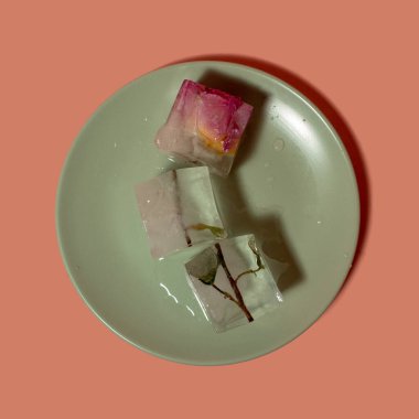 Tabakta buz küpleri içinde pembe çiçeğin yaratıcı düzenlemesi. Güneşli gün konsepti. Boşluğu kopyala