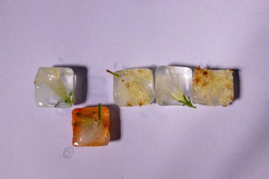 Renkli çiçeklerin pastel mor arkaplandaki buz küplerinde yaratıcı bir düzenleme. Güneşli gün konsepti.