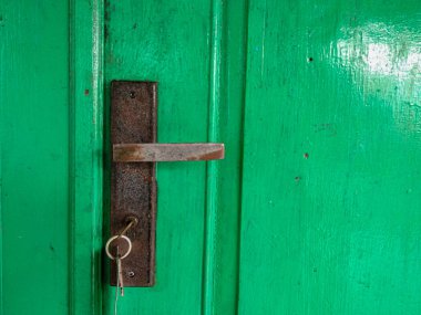 Üzerinde anahtar olan paslı yeşil kapı kolu.