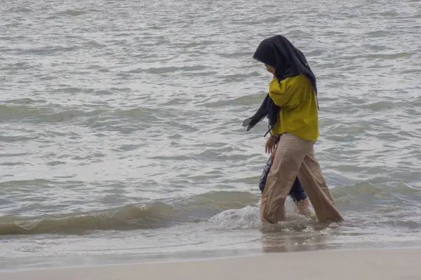 Lampung Timur, Endonezya - 02 Ocak 2025: Sahilde yürüyen iki genç Asyalı kız. İnsanlar okul tatillerinde plaja tatile giderler.