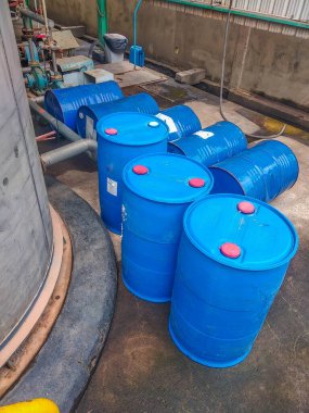 Endüstriyel ekipmanların yanında kırmızı kapaklı büyük mavi plastik fıçılar dizilmiştir.