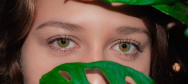 Yüzünü yapraklarla kaplayan genç ve güzel bir kadının yüzünü yakından çek. Doğal makyajlı kadın portresi