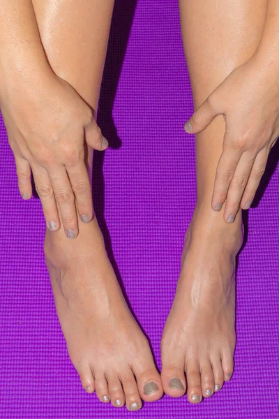 Female feet with pedicure and manicure on purple background.