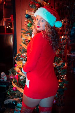 Noel Baba kıyafetli güzel bir kadının portresi Noel ağacının arkasında..