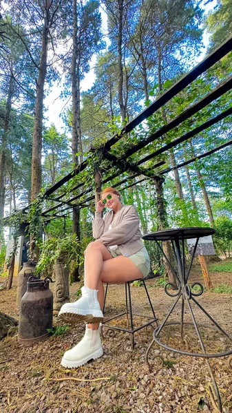 Parkta bir bankta oturan ve doğanın tadını çıkaran güzel genç bir kadın. Güneş gözlüğü takıyor. Başka yere bakıyorum..