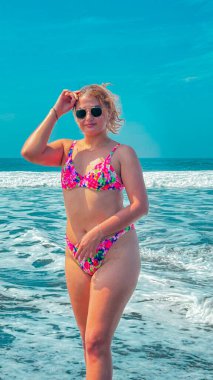 Güneşli bir günde, plajda pembe bikinili ve güneş gözlüklü güzel bir kadın. portre.