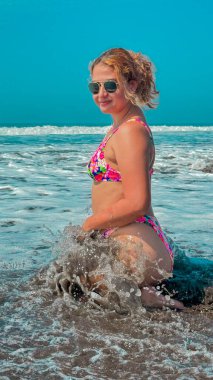 Bikinili güzel bir kadın denizde bir dalgada oturuyor..